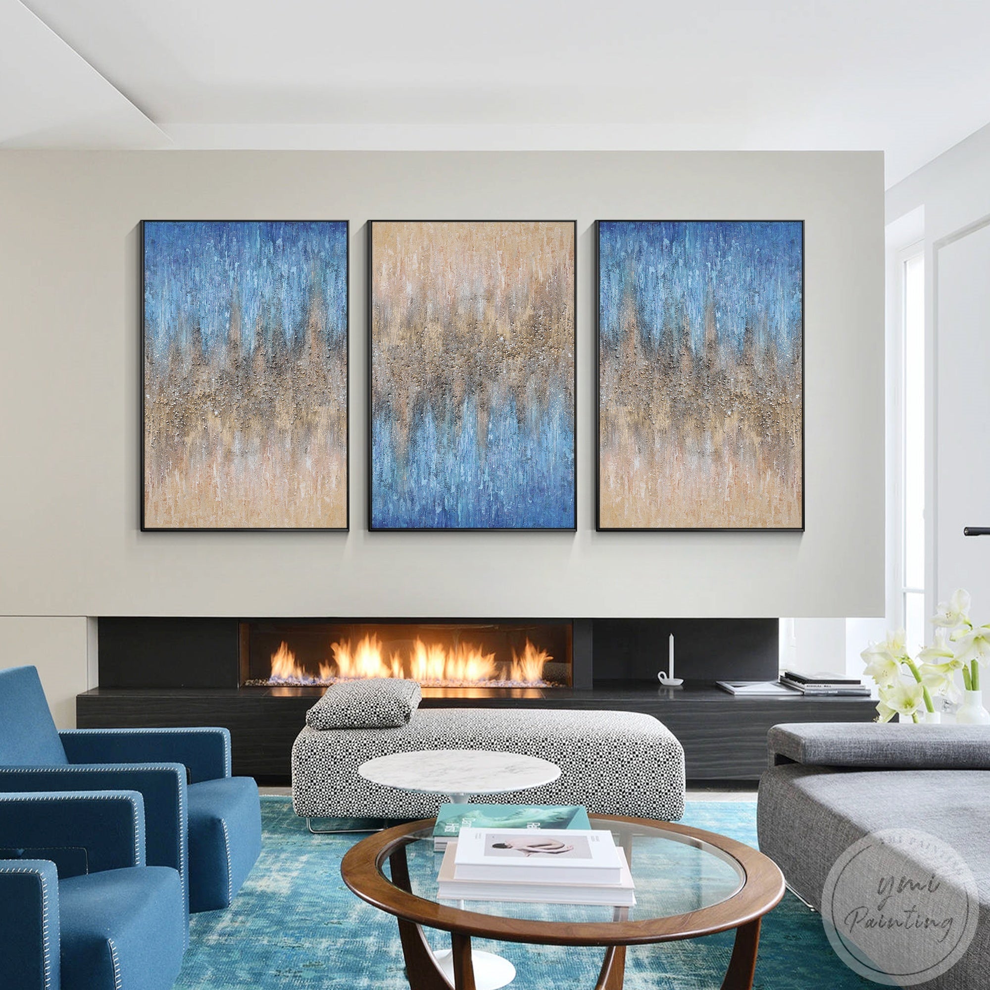 Triptych artwork with shimmering gold details and prismatic crystal embellishments on a beige and blue background over a fireplace in a bright living room.